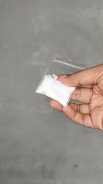 Closeup of asian or indian person hand holding cocaine or heroin drug powder inside small zip bag isolated on white background with copy space. Consuming narcotic substance concept.