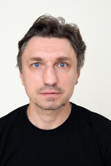 Fototapeta premium close up portrait of middle aged man with blue eyes and stubble in black t-shirt looking at camera with slight smile, white background headshot