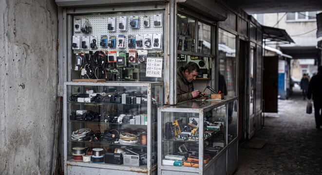Street electronics repair kiosk in a weathered urban passage, Eastern Europe editorial-like