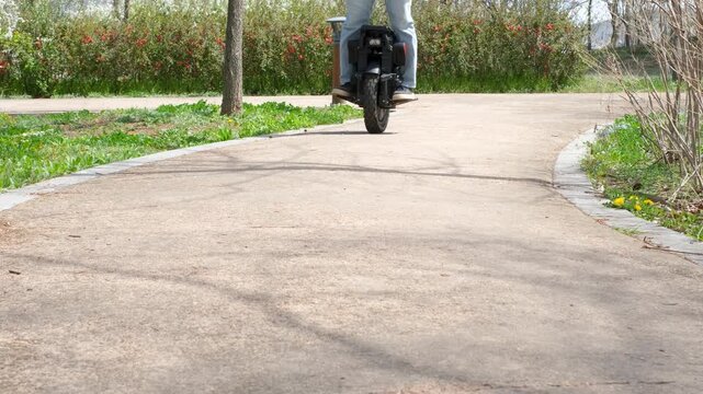 A man in blue jeans and sneakers rides an electric unicycle.