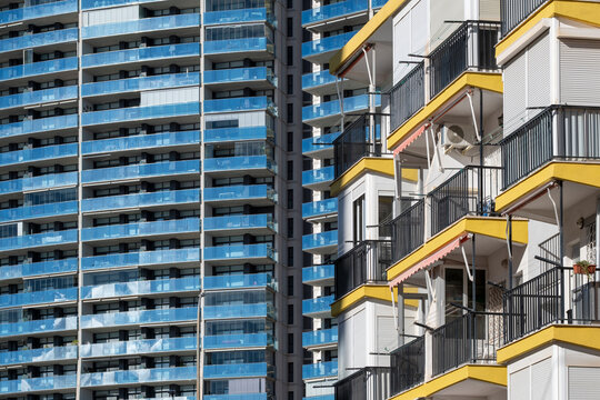 Yellow balcony edges cross a dense building facade in Benidorm, Spain, where modern urban architecture meets blue glass, sky and geometry