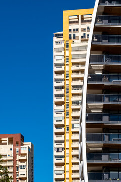 A yellow balcony line climbs a modern residential building in Benidorm, Spain, sharpening urban architecture and facade geometry against blue sky