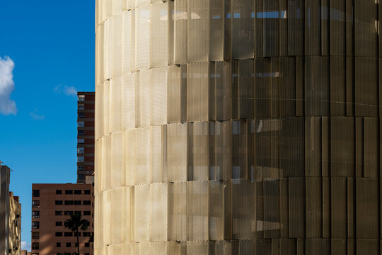 Golden mesh and blue sky divide a modern building facade in Benidorm, Spain, reading urban architecture through texture, shadow and geometry