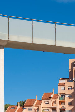 An elevated walkway cuts through blue sky in Benidorm, Spain, framing modern urban architecture and residential building facade geometry below