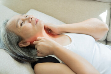 Fototapeta premium Worried mature Asian woman suffering from neck pain and discomfort after waking up in bed