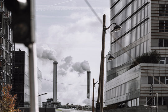 Smoke rises between chimneys and office facade towers in an urban cityscape of Paris, France, where industry and architecture meet a hard skyline