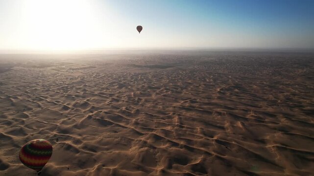 Drone flies around balloons with tourists over the sand dunes of the desert in Dubai