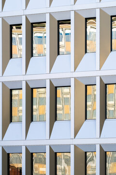 Sunlit glass window bays shape a modern building facade, giving urban architecture an abstract geometry of shadow, pattern and clean detail