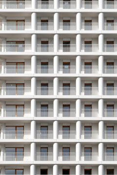 Repeating balconies define a modern building glass facade, where urban architecture becomes abstract geometry through white pattern and measured detail