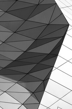 Triangular panels and glass edges wrap a modern building facade, reducing urban architecture to abstract geometry, shadow pattern and detail