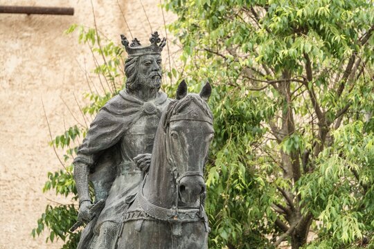 Bronze equestrian statue of King Alfonso VIII of Castile framed by green tree leaves and branches against an ochre wall in Cuenca Spain