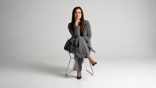 Portrait of a cheerful young businesswoman sitting in a chair against white background.