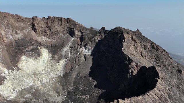 Close-up aerial view of the rugged crater rim of Pico do Fogo, Cabo Verde, showing colorful mineral deposits, and layered volcanic rock formations