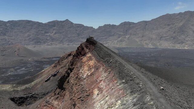 High-altitude drone shot of a group of trekkers standing on the narrow, rugged crater rim of Pico do Fogo