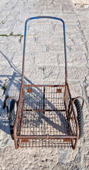 Fototapeta premium High angle view of an old weathered rusty metal wire cart with two wheels standing on a stone paved pier.