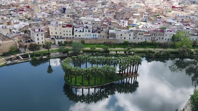 Aerial drone view of palm island reflected in calm water with historic Fez cityscape in background Morocco ideal for travel and documentary projects
