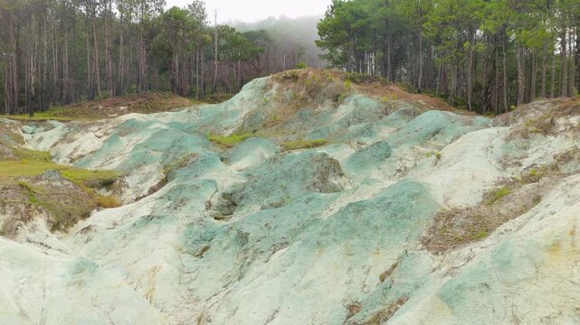 Low-altitude aerial sideways flight past Blue Soil Hills in Sagada reveals intimate close-up of surreal blue-green and white mineral clay mounds framed by misty pine forest