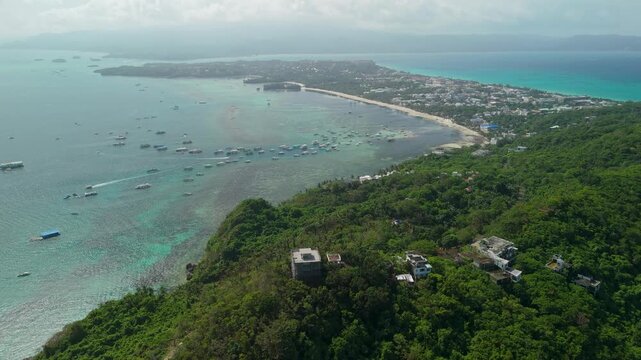 Slow aerial tilt-up from Mount Luho revealing full Boracay Island with Bulabog Beach, dozens of moored bangka boats, White Beach coastline, and ocean panorama, Philippines