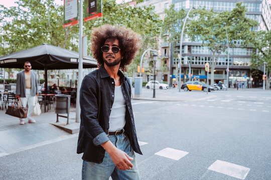 Latin american man with afro hair and sunglasses walking on city crossing street in casual style.