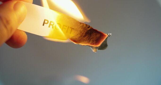 Close-up of a paper strip with the word &ldquo;profit&rdquo; burning, symbolizing financial loss, business risk, market pressure, economic crisis, and declining revenue.