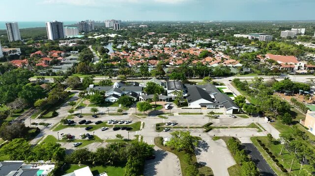 High-altitude aerial of the Naples United Church of Christ in Southwest Florida, nestled among red-roofed homes, manicured landscapes, and views toward the Gulf of Mexico.
