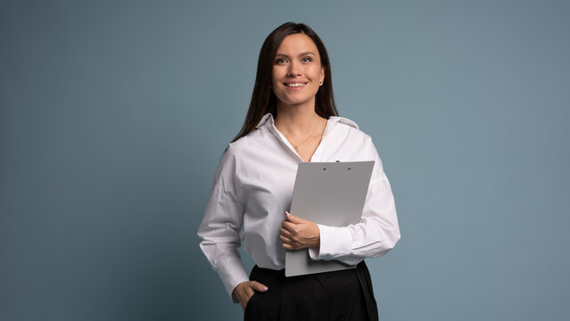 Middle-aged happy businesswoman holding folders on blue