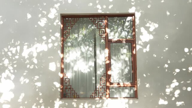 Chinese window frame casting sunlight shadows on white wall