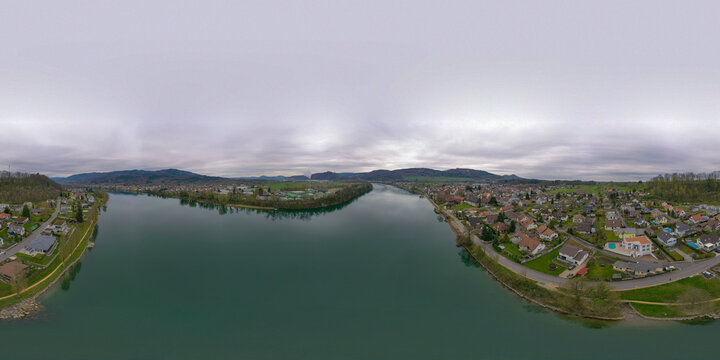 Aerial view of the Rhine River flowing through the town of Bad Sackingen with residential houses and green hills under an overcast sky in Bad Sackingen, Baden-Wurttemberg, Germany.