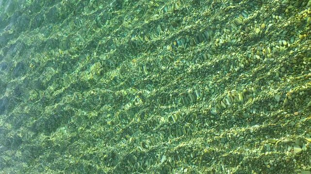 Transparent water creates abstract patterns and wavy refractions over a bed of smooth, varied pebbles, offering a peaceful and natural background texture