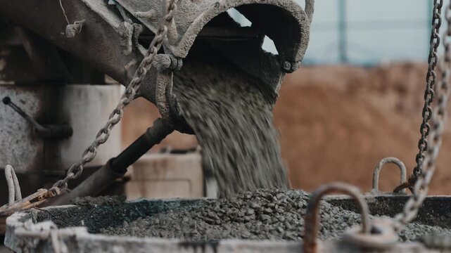 Concrete pouring from mixer chute into suspended construction bucket close up