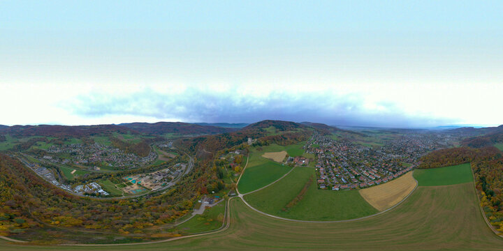 Aerial view of Ruine Pfeffingen castle ruins surrounded by lush green hills, residential houses, and autumn-colored forests in Pfeffingen, Basel-Landschaft, Switzerland.