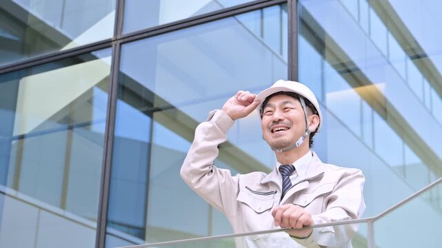 [スローモーション]都会のビル背景で未来を見つめる建設業や施工管理、ビルメンテナンスのヘルメットを被った作業着の40代の男性　キャリアと成長イメージの動画　左にコピースペースあり