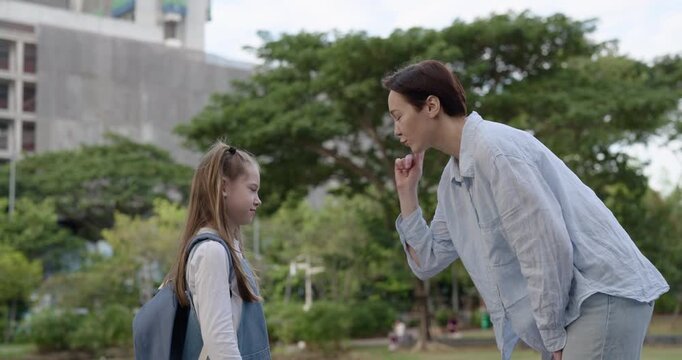 Portrait of serious mother rebukes little girl student for learning failures in green park. Woman threatens by finger to daughter pupil in urban garden