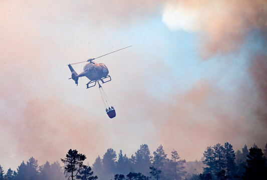 Helicopter carrying water bucket for extinguishing fire while flying in sky