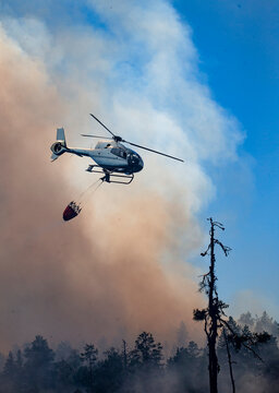 Low angle view of helicopter carrying water bucket for extinguishing fire while flying in sky against smoke