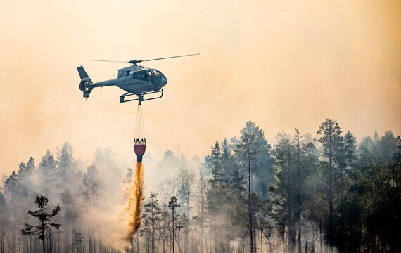 Drone view of helicopter pouring sand down with bucket against smoky sky and trees
