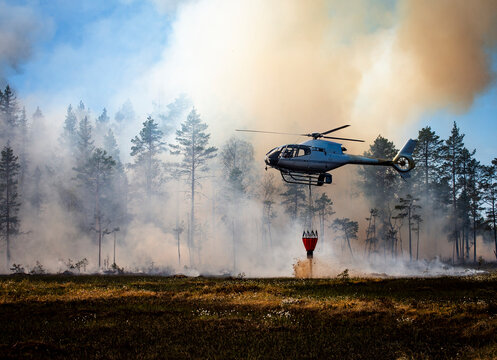 Helicopter pouring sand with bucket on land against smoky sky and trees