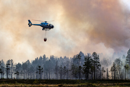 Helicopter flying with water bucket in smoky sky above forest