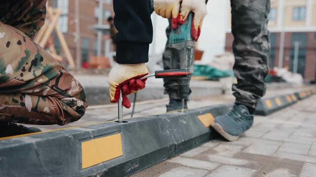 Worker drilling and fastening rubber parking wheel stop on tiled pavement