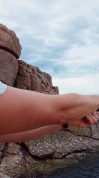 Vertical video. Young Woman Casting Spinning Rod From Rocky Tropical Coast Near Calm Ocean Under Dramatic Cloudy Sky, Slow Motion Recreational Fishing Adventure
