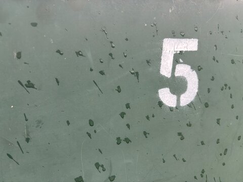 A large white numeral 5 is spray-painted onto a weathered, dark green metal surface, showing signs of age and wear.