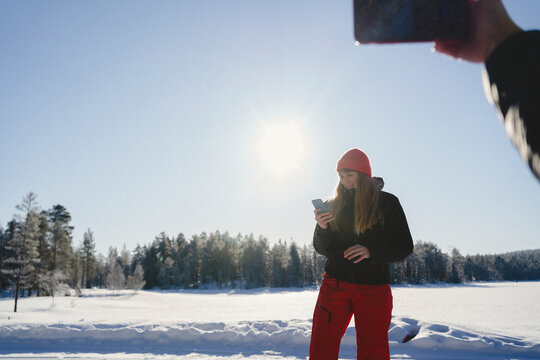 Woman using smart phone while standing in snow at sunny day