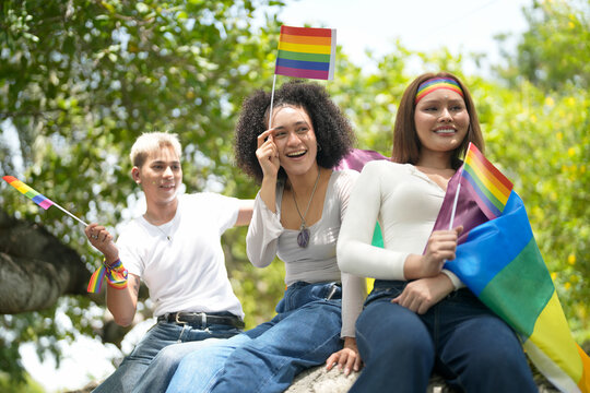 Three friends proudly hold rainbow flags celebrating LGBTQ+ pride outdoors