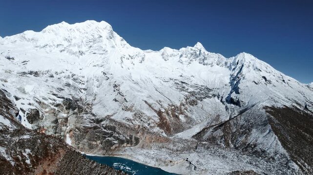 A sweeping view of the massive snow-covered Manaslu mountain range glistening under a clear blue sky in Nepal.