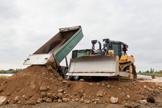 Bulldozer beside truck dumping dirt on road against cloudy sky