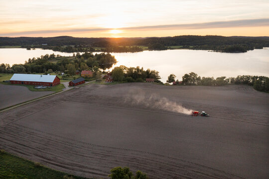 Drone point of view of tractor on agricultural field near lake at sunset