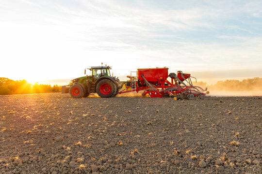 Tractor pulling seed drill machine on field against cloudy sky at sunny day