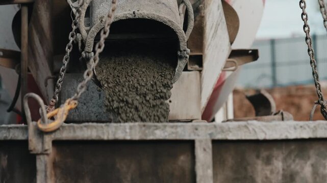 Concrete pouring from mixer chute into construction bucket close up