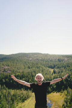 Happy man standing with arms outstretched against rural landscape