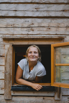 Portrait of smiling woman leaning out from her cabin window in forest